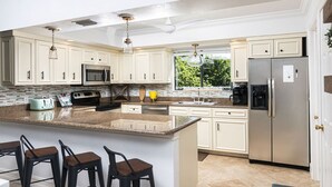 A modern kitchen with white cabinets, stainless steel appliances, a granite countertop, and a large island with bar stools. - Villa Palma - Walk to Beach Pool House! Location Location Location (Naples)