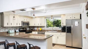 A modern kitchen with white cabinets, stainless steel appliances, a granite countertop, and a large island with bar stools.