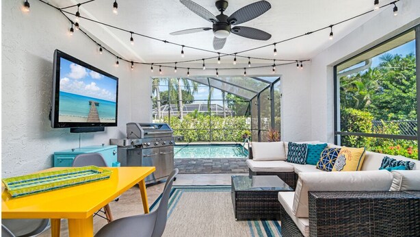 A sunlit patio with a pool, outdoor seating, a grill, and a TV mounted on the wall. - Villa Palma - Walk to Beach Pool House! Location Location Location (Naples)
