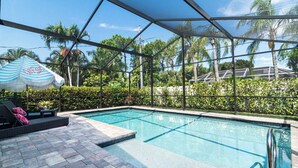 A swimming pool with a glass enclosure, surrounded by lush greenery and palm trees. - Villa Palma - Walk to Beach Pool House! Location Location Location (Naples)