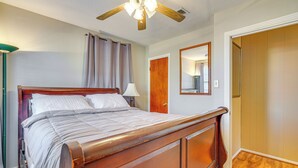 Een slaapkamer met een houten bed, een plafondventilator, een nachtkastje met een lamp, een deur en een spiegel.