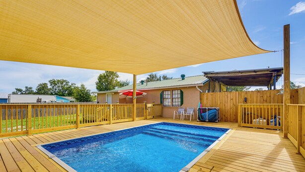 Een houten terras met een zwembad, een overdekt gedeelte met een rode parasol en een houten omheining.