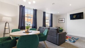 A modern living room with a round table, green chairs, a grey sofa, and a TV mounted on the wall. - WhiskAwayStays  Victoria House  Apartment 4 (Worcester)