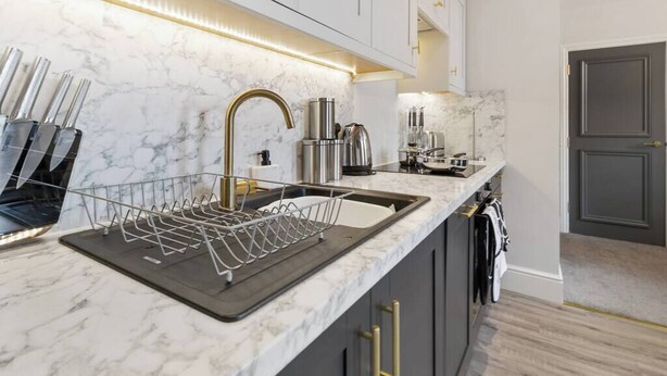 A modern kitchen with a marble countertop, stainless steel appliances, and gold handles on the cabinets. - WhiskAwayStays  Victoria House  Apartment 4 (Worcester)