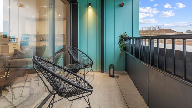 Ein Balkon mit zwei schwarzen Stuhlgestellen, einem Blumentopf und Blick auf Gebäude im Hintergrund.