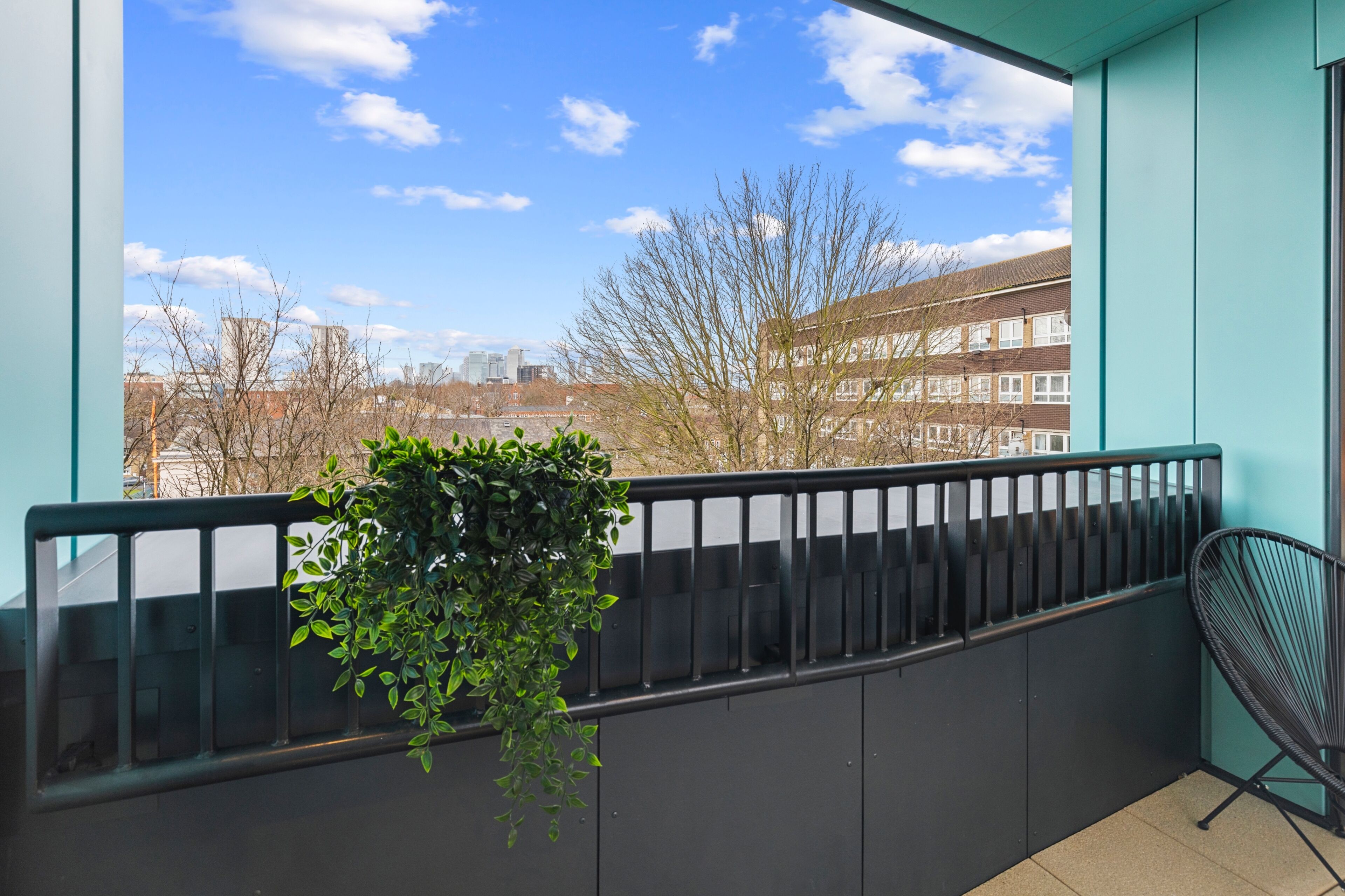 A balcony with a view of buildings and trees, a potted plant, and a chair.