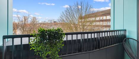 A balcony with a view of buildings and trees, a potted plant, and a chair.