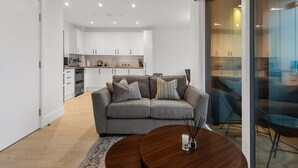 Ein modernes Wohnzimmer mit einem grauen Sofa, einem runden Couchtisch und einer Glaswand, die in einen Essbereich führt.