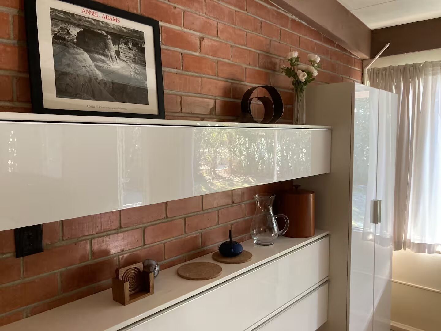 Une pièce avec un mur en briques, un tableau encadré, un vase de fleurs et un meuble contenant des objets décoratifs.