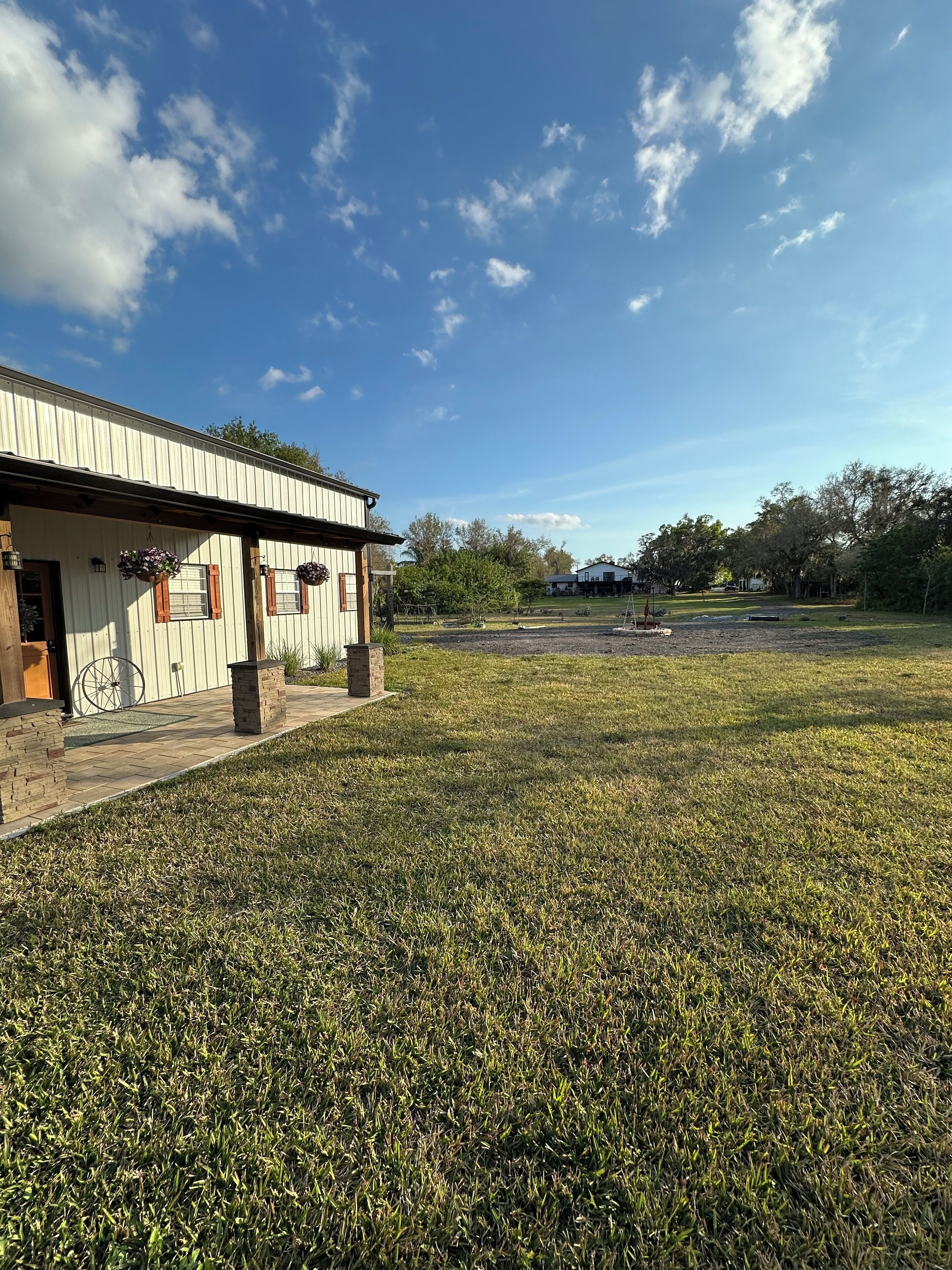 A building with a corrugated metal exterior, a brick foundation, and a small porch area with hanging flower baskets.