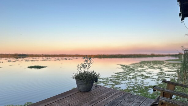 A wooden deck with a potted plant and a chair, overlooking a calm body of water with distant land.