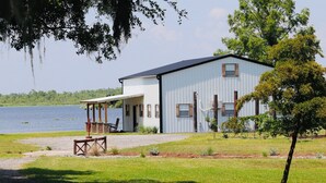 A single-story building with a covered patio area, a gravel driveway, and a view of a lake.