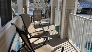 A covered porch with two rocking chairs, a table, and a potted plant. - Spacious 4-bedroom condo steps from The Starboard in Dewey Beach (Dewey Beach)