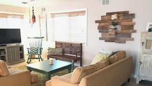 A living room with a sofa, armchairs, a coffee table, a TV, and a decorative wall piece. - Spacious 4-bedroom condo steps from The Starboard in Dewey Beach (Dewey Beach)