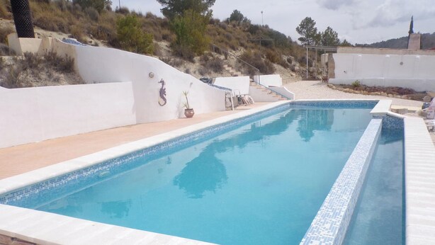 A rectangular swimming pool with a tiled edge, surrounded by a white wall and a wooden deck. - Apartment Sleeps 4 With Private Pool (Jumilla)