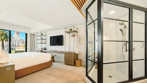 Een moderne slaapkamer met een groot bed, een bureau, een televisie, een inloopdouche en uitzicht op de stad.