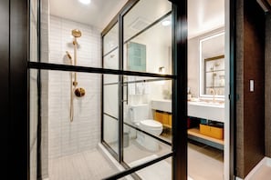 A modern bathroom with a glass-enclosed shower, a white toilet, and a vanity with a mirror and sink.