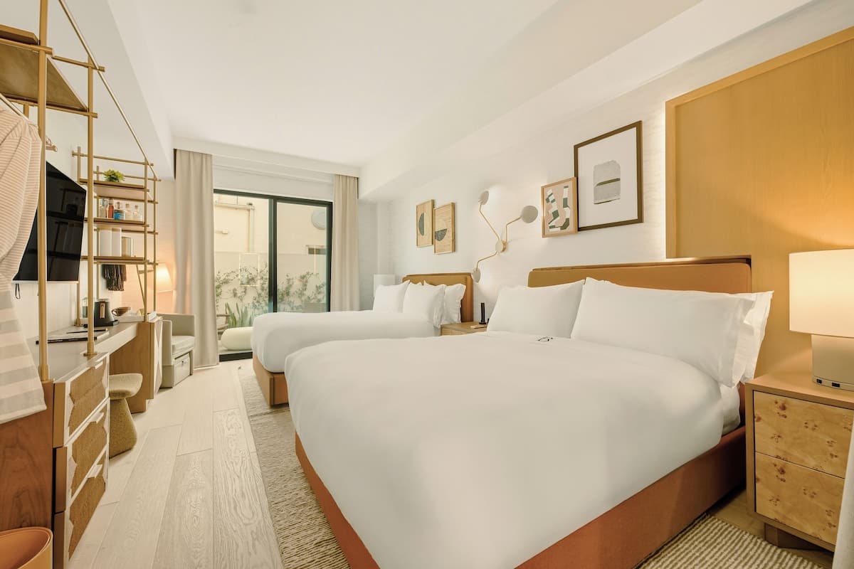 A hotel room with two beds, a desk, a chair, a TV, and a large window.