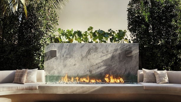 A modern outdoor seating area with a built-in fire feature, surrounded by lush greenery. - The Bower Coronado (Coronado)