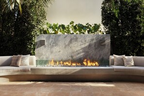 A modern outdoor seating area with a built-in fire feature, surrounded by lush greenery. - The Bower Coronado (Coronado)