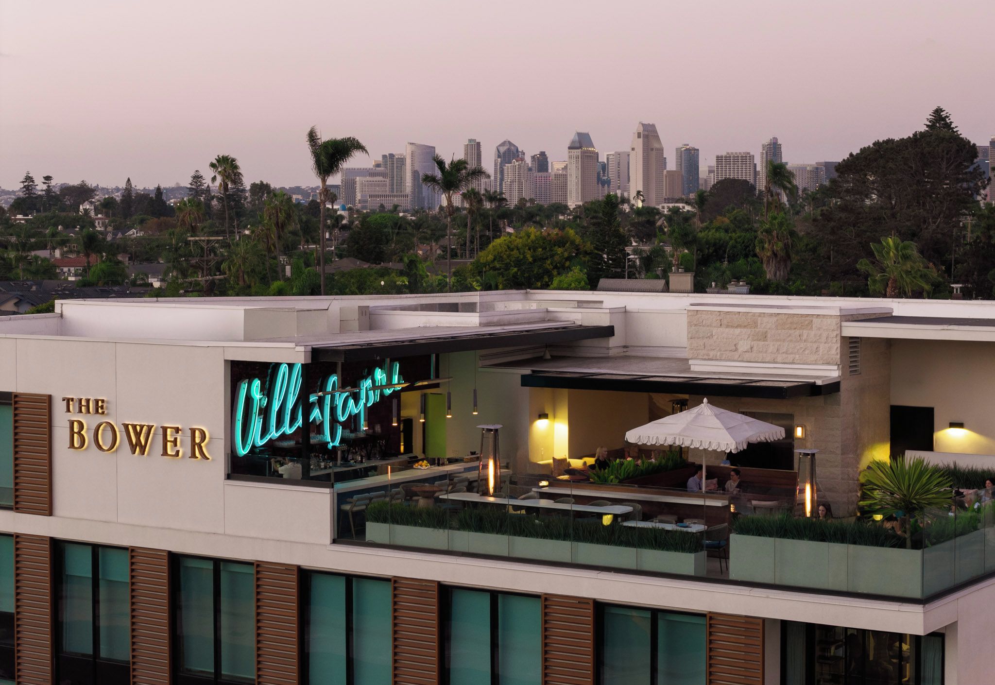 A rooftop bar with a neon sign, overlooking a city skyline.