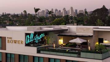A rooftop bar with a neon sign, overlooking a city skyline.