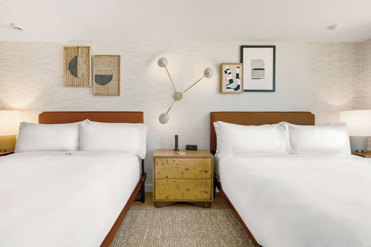 A hotel room with two beds, a nightstand with a lamp, and wall art.