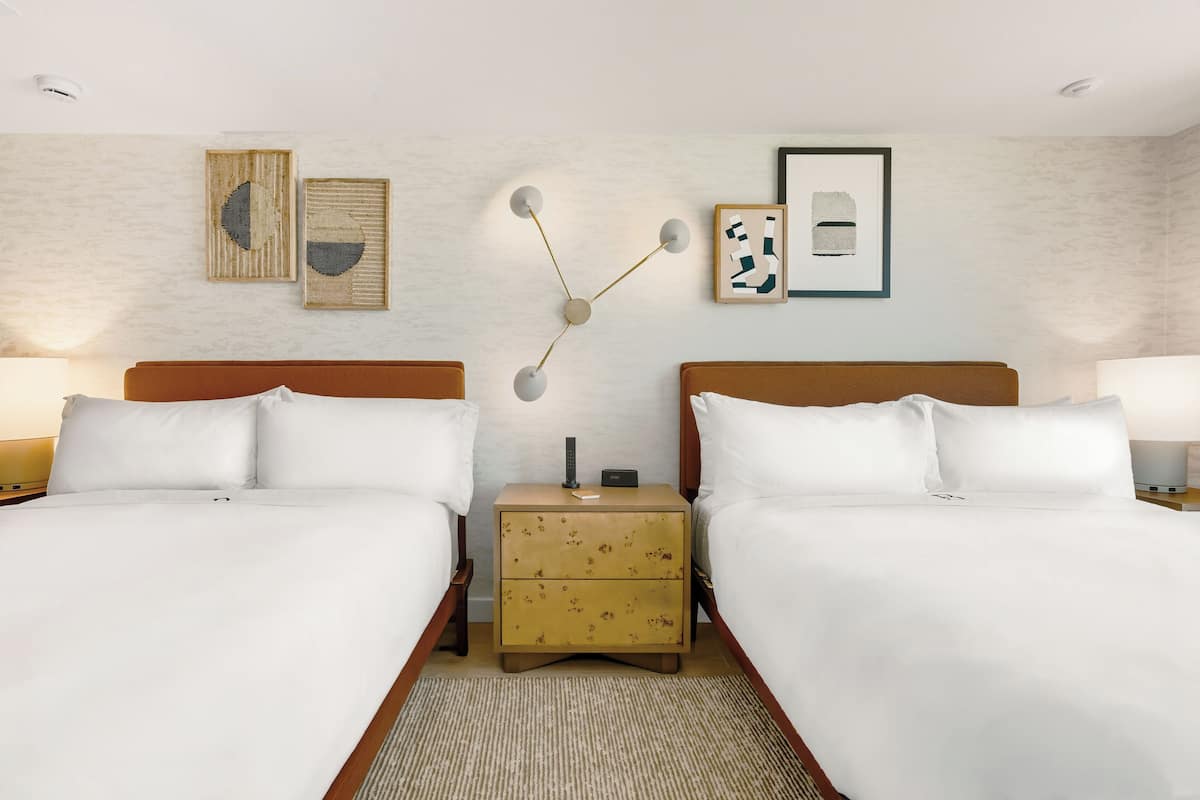 A hotel room with two beds, a nightstand with a lamp, and wall art.