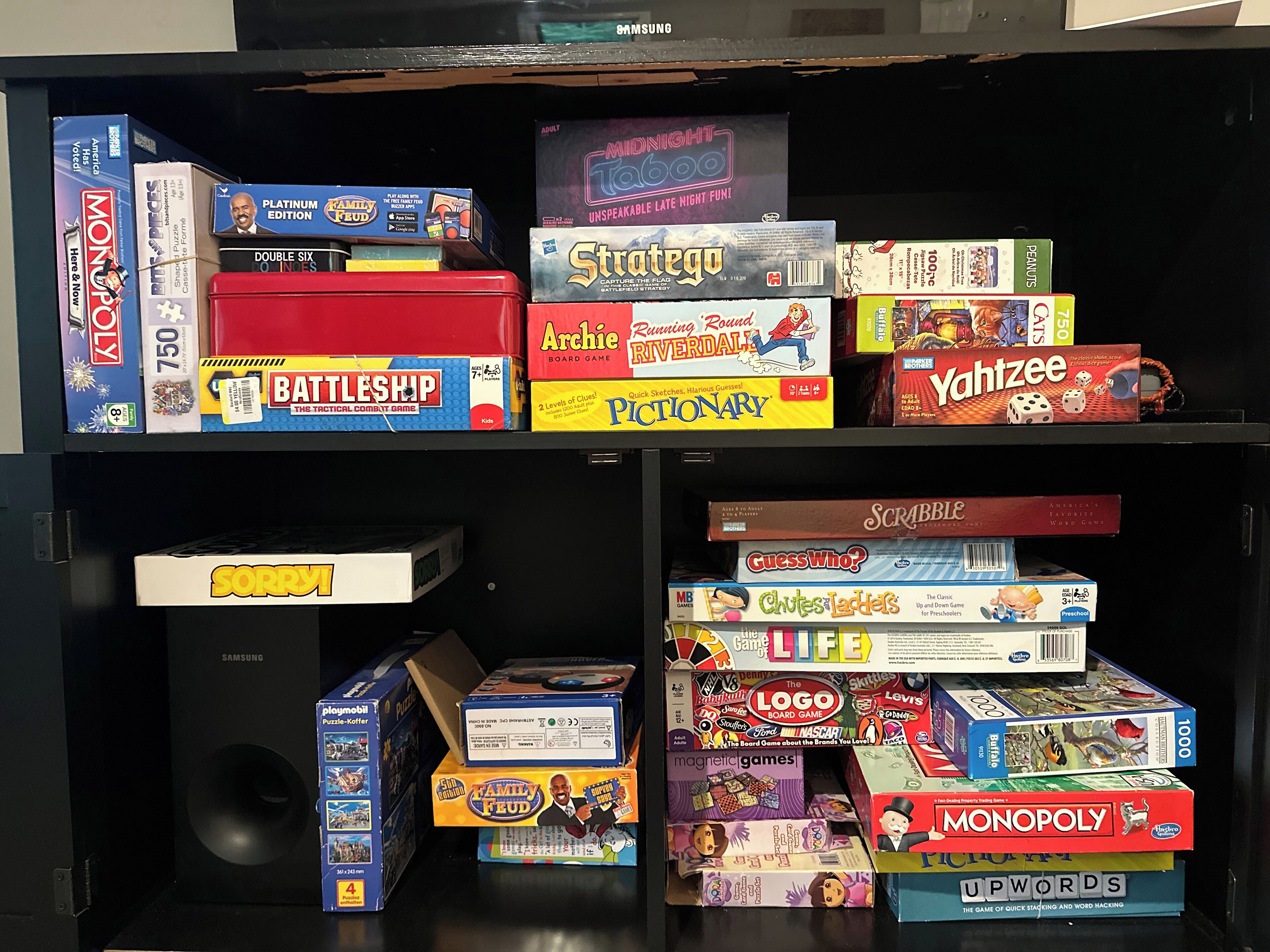 A shelf with various board games stacked horizontally.