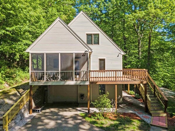 Une cabane à deux étages dotée d’un balcon et d’une terrasse en bois, entourée d’arbres.