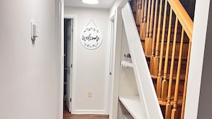 A hallway with wooden flooring, white walls, a welcome sign, and a wooden staircase.