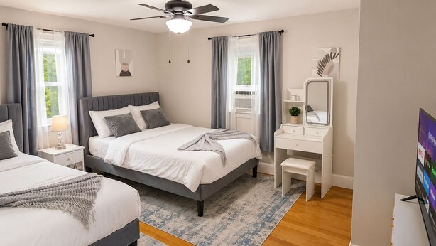 A modern bedroom with a bed, bedside tables, a desk, a mirror, a ceiling fan, and a TV.