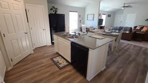 A modern kitchen with a dishwasher, a sink, and a dining area with chairs and a table. - Mac's Cozy Farmhouse (Stillwater)