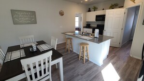 A modern kitchen with white cabinets, a central island, and a dining area with white chairs and a dark table. - Mac's Cozy Farmhouse (Stillwater)