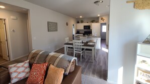 A living room with a brown sofa, a dining table with chairs, and a kitchen in the background. - Mac's Cozy Farmhouse (Stillwater)