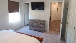 A bedroom with a bed, a dresser, a ceiling fan, a TV, and a window with blinds. - Mac's Cozy Farmhouse (Stillwater)