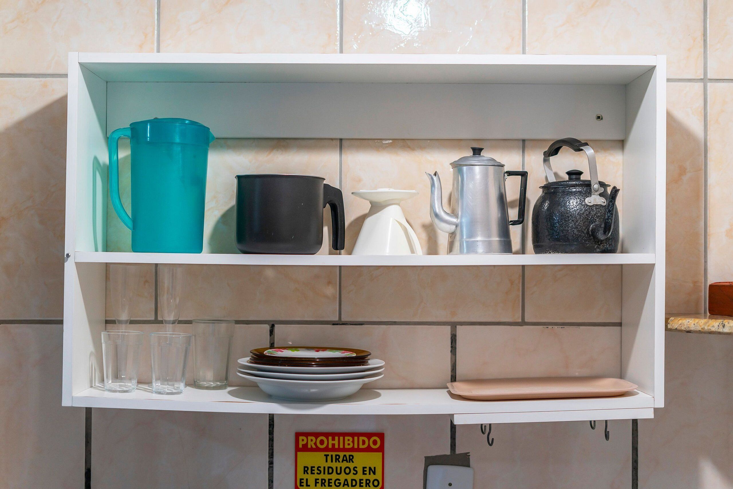 A kitchen shelf with various kitchenware including a teal pitcher, black mug, white teapot, and a black kettle.