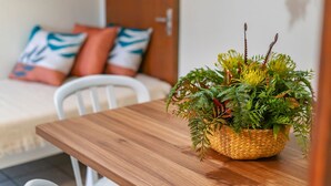 A wooden table with a woven basket containing green foliage. A white chair is positioned in front of the table. - AP 26 Ala Canto Gran Residencial Solavir (Bombinhas)