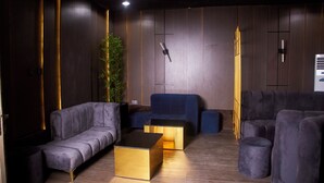 A modern living room with a sofa, two gold coffee tables, and a blue accent chair. - De Mipos Luxury Suites (Abuja)