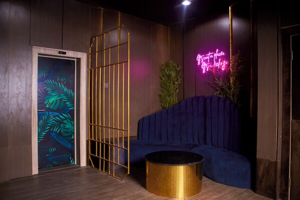 A modern room with a blue sofa, a gold-framed window, and a neon sign. - De Mipos Luxury Suites (Abuja)