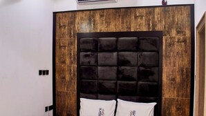 A bedroom with a large bed, a wooden headboard, an air conditioning unit, and a small rug. - De Mipos Luxury Suites (Abuja)