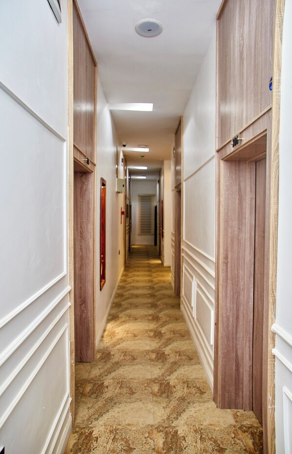 A hotel hallway with wooden paneling, a marble floor, and a ceiling light. - De Mipos Luxury Suites (Abuja)
