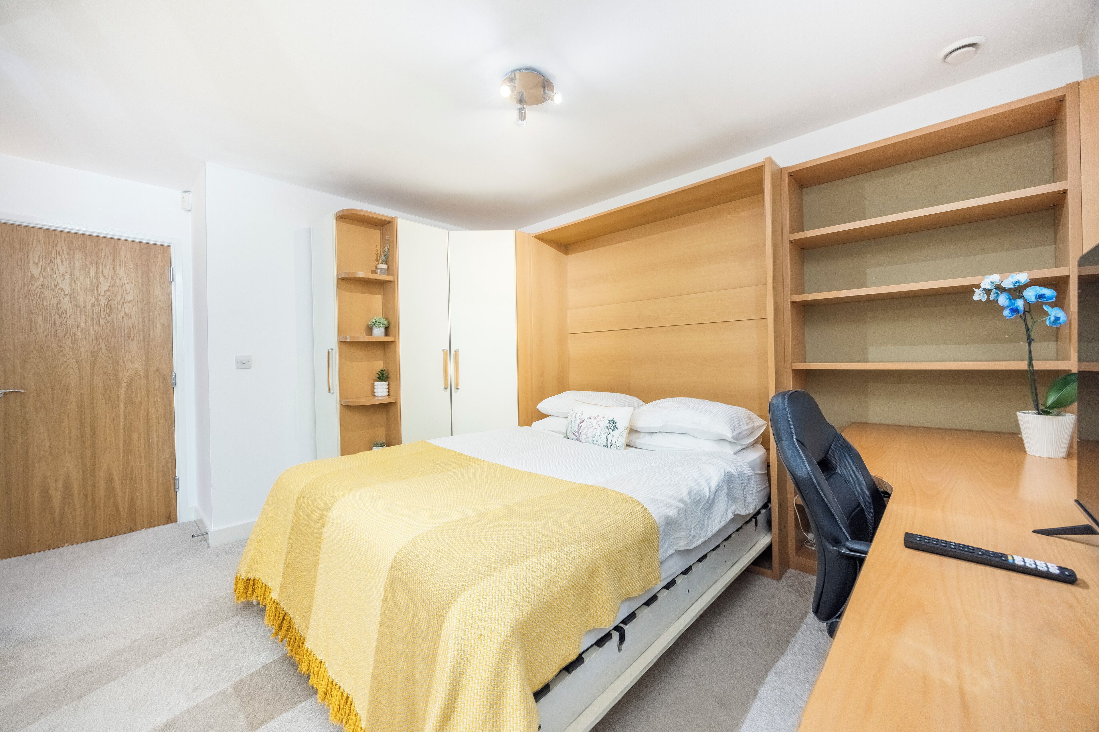 Une chambre à coucher comprenant un lit, un bureau, une chaise et des étagères intégrées.