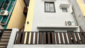 Un edificio residencial de varios pisos con techo plano, un balcón con barandilla a rayas y un equipo de aire acondicionado en la pared exterior.