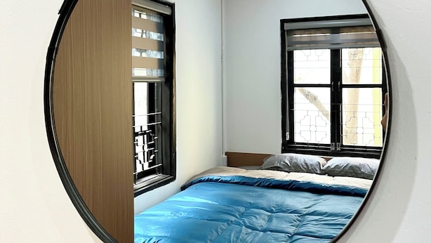 Una habitación con una cama, un ventanal con rejas decorativas y un espejo en la pared.