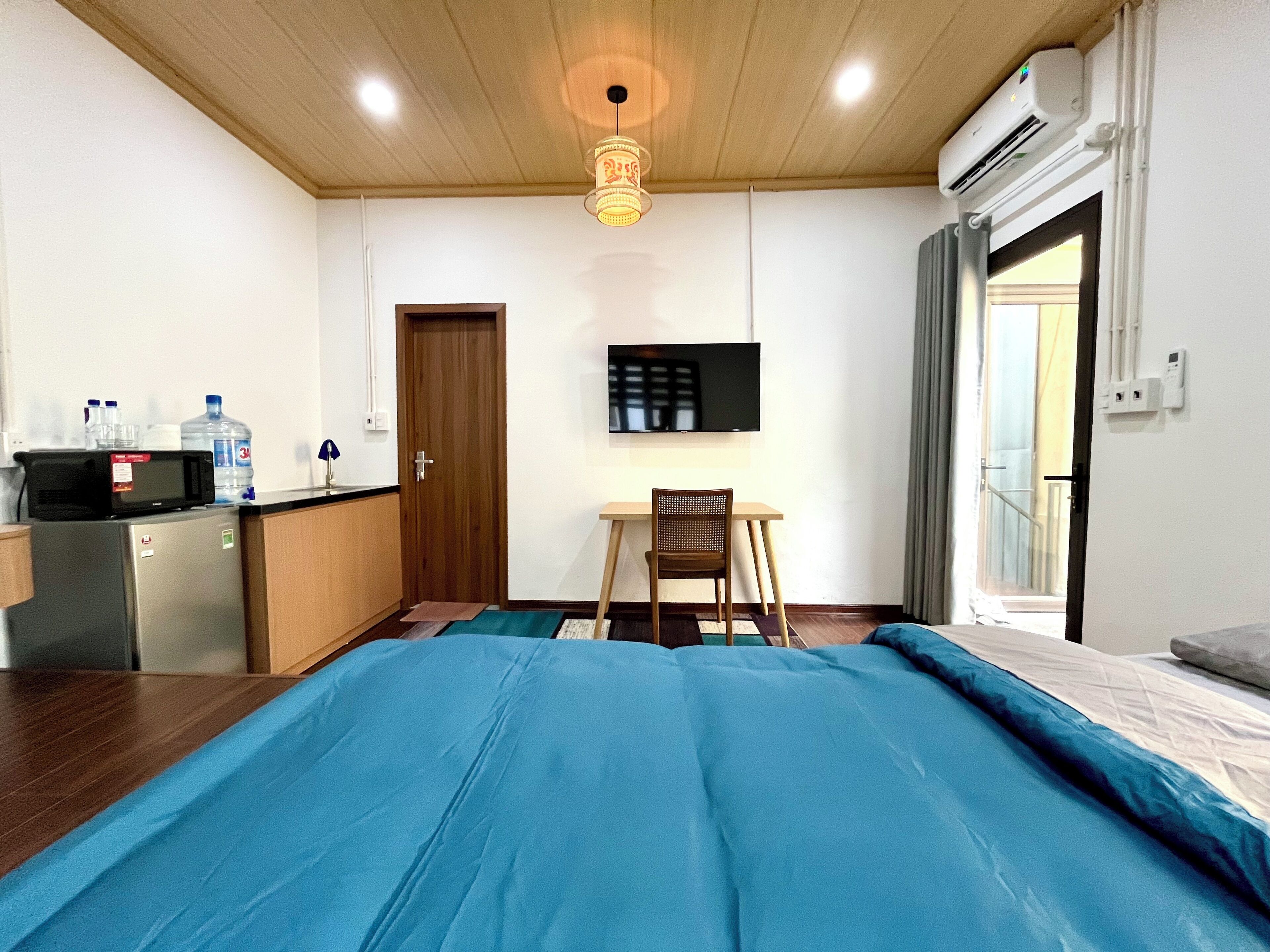 Una habitación con cama, escritorio, silla, televisor y kitchenette.