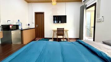 Una habitación con cama, escritorio, silla, televisor y kitchenette.