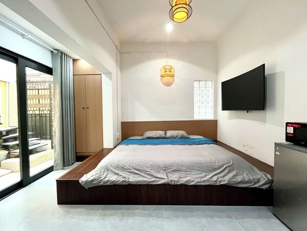 A modern bedroom with a large bed, a television, and a sliding glass door leading to an outdoor area.