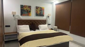 Une chambre moderne avec un grand lit, deux lampes fixées au mur et deux tableaux abstraits.