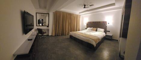 A hotel room with a bed, a desk, a chair, a television, and a large window with curtains.